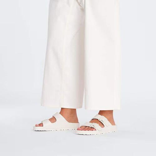 Cream sandals worn with white pants on a light gray background