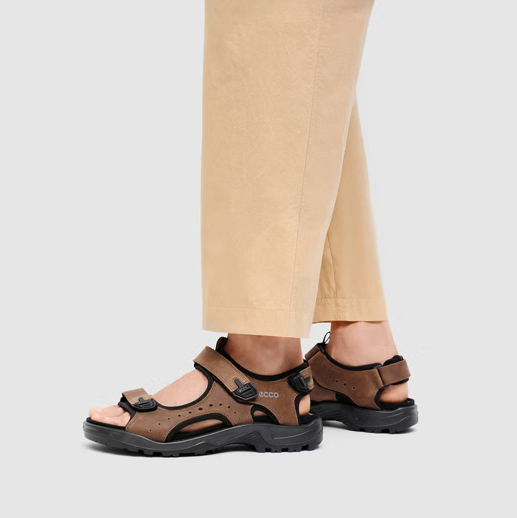Brown sandals worn with beige pants on a light gray background
