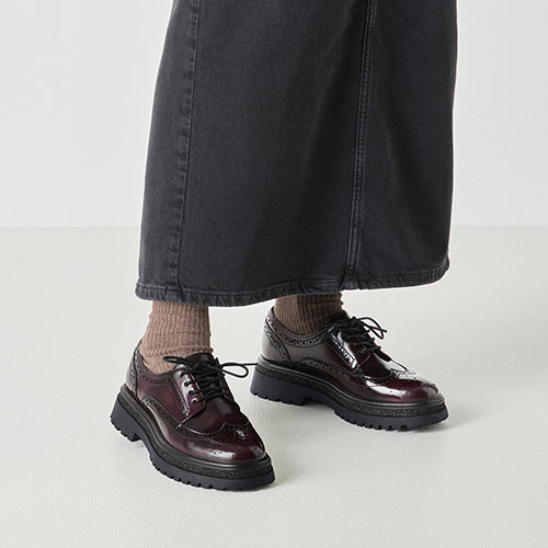 Person wearing burgundy brogues with thick soles on a light gray background