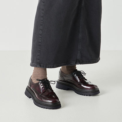 Person wearing burgundy brogues with thick soles on a light gray background