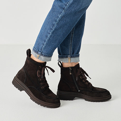 Brown suede boots worn with rolled-up blue jeans on a light gray background