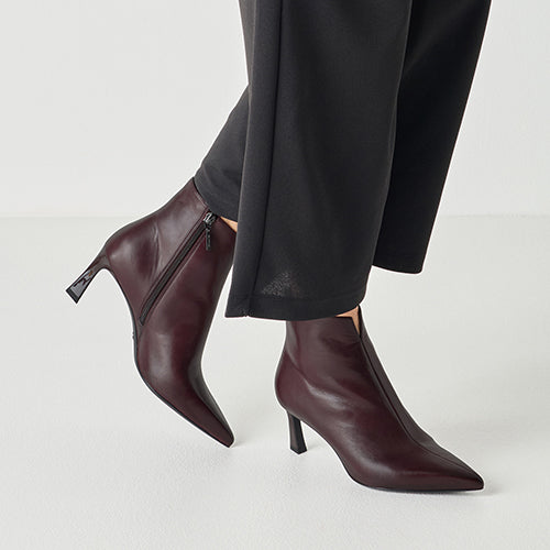 Burgundy ankle boots with a high heel worn with black pants on a light gray background