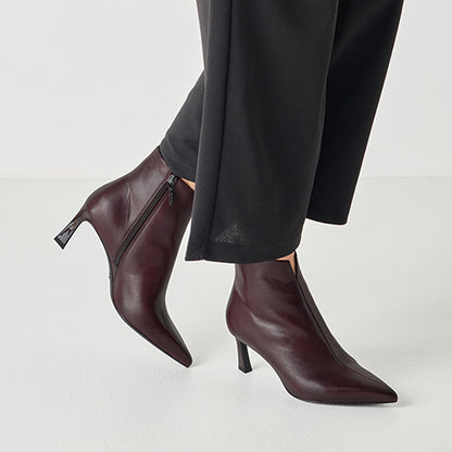 Burgundy ankle boots with a high heel worn with black pants on a light gray background