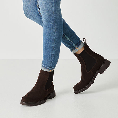 Brown Chelsea boots worn with blue jeans on a white background