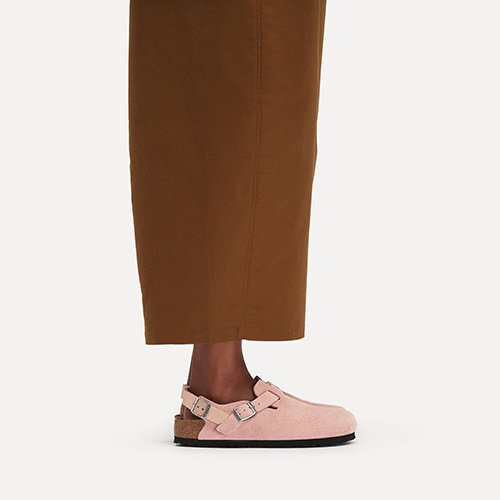 Pink Backstrap birkenstock suede shoes with cork sole worn with brown trousers on a white background
