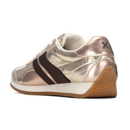 A metallic rose gold trainer with dark brown three-stripes, a white midsole, and a brown gum outsole, shown from a side-rear angle on a white background.