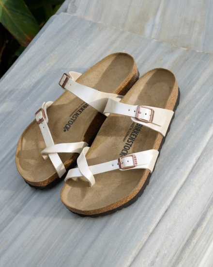 Pair of white sandals with brown soles on a light gray surface
