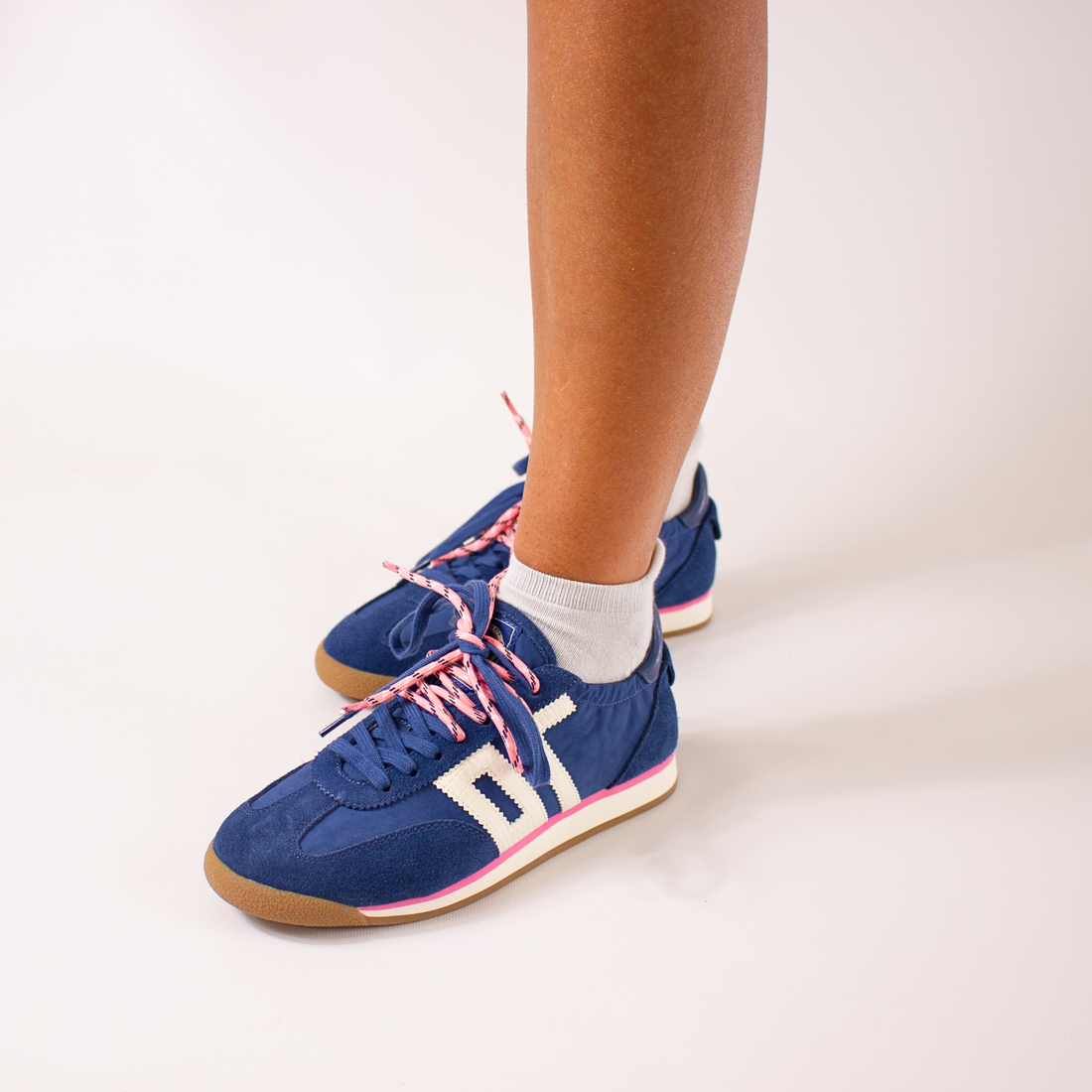Blue retro trainers with pink laces worn by a person on a light background
