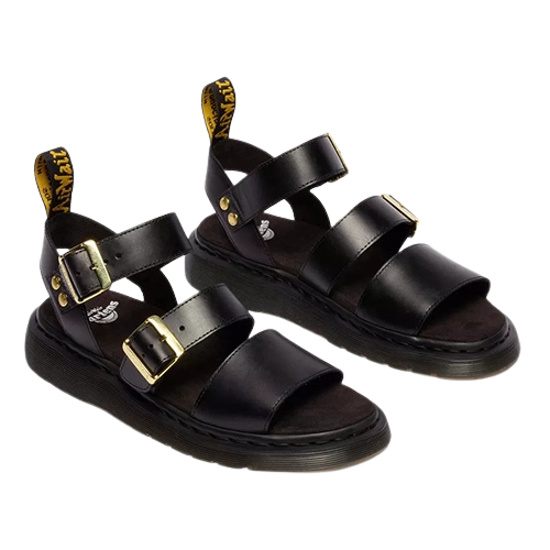 Black Dr Martens sandals with gold buckles on a white background