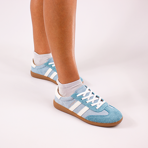 Light blue trainers with white stripes worn by a person on a light gray background