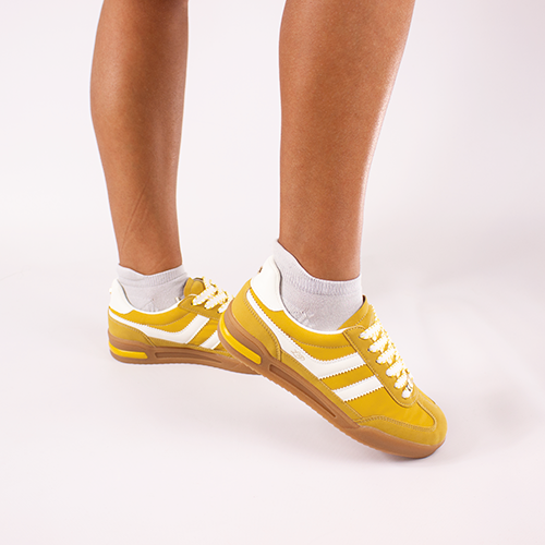 Yellow trainers with white soles worn on a light gray background