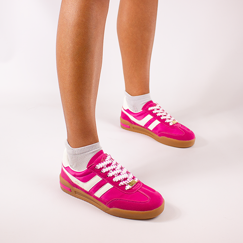Pink trainers with white stripes worn by a person on a light gray background