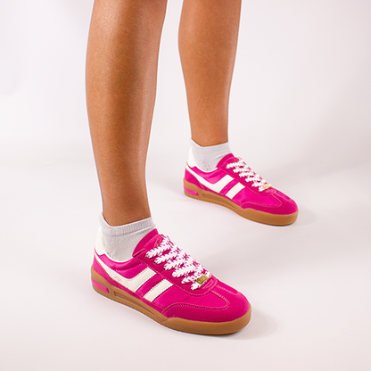 Pink trainers with white stripes worn by a person on a light gray background