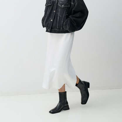 Person wearing a black denim jacket, white skirt, and black shoes on a white background