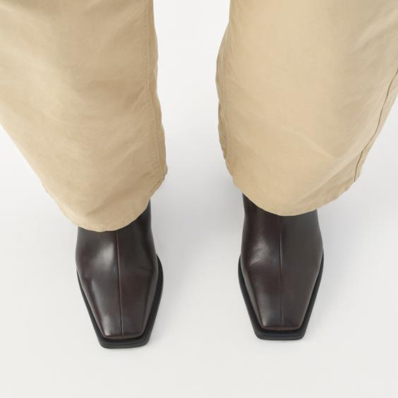 Brown leather boots worn with beige pants on a white background