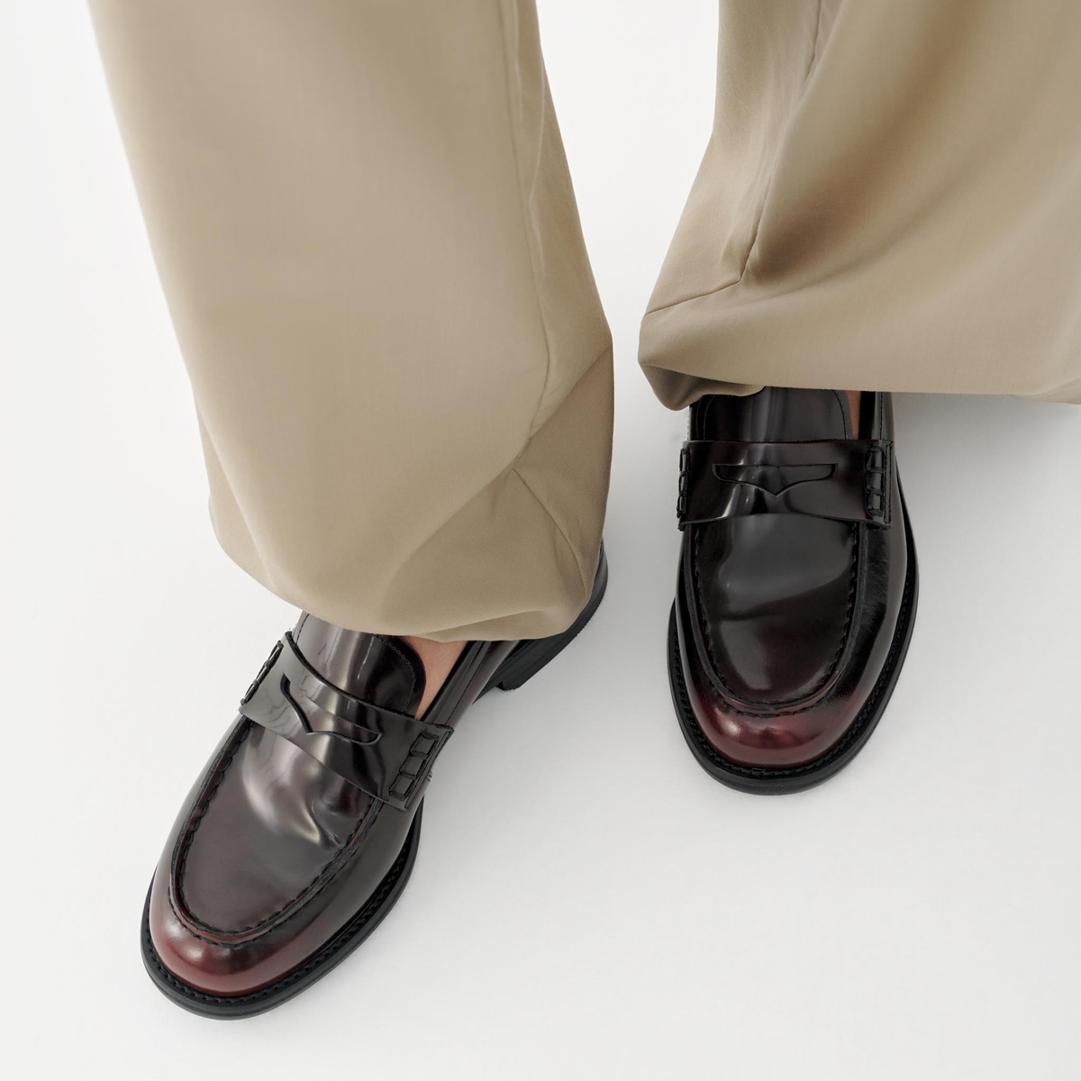 Burgundy loafers worn with beige pants on a white background
