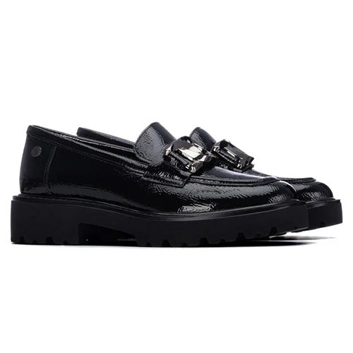 A pair of black patent leather slip-on loafers with chunky lug soles and a decorative silver-tone buckle detail across the vamp, shown against a plain white background.